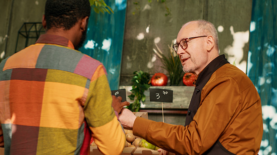 Small business owner selling fresh homegrown products at farmes market, stand holder presenting organic fruits and veggies. Local vendor putting natural colorful ripe bio produce.