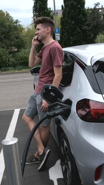Man talking on smartphone while waiting for his electric car to charge