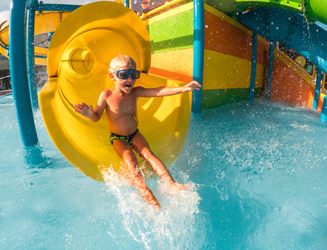 Happy little boy water sliding in a water park in Croatia. Wearing swimming goggles and having fun splashing the water.