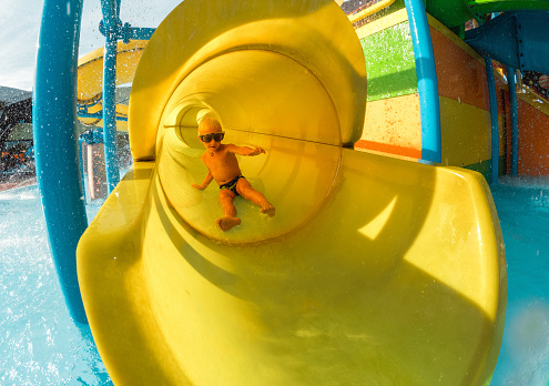 Happy little boy water sliding in a water park in Croatia. Wearing swimming goggles and having fun splashing the water.