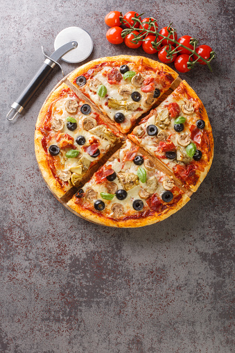 Pizza capricciosa with white mushrooms, ham, artichoke, tomatoes, olives, parmesan and mozzarella on wooden board on the table. Vertical top view from above