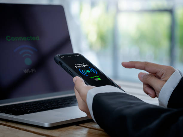istock personal hotspot technology concept. The words personal hotspot, internet sharing icon and green activated button on mobile smart phone screen in hand, connecting wi-fi network to laptop computer. 1450267009