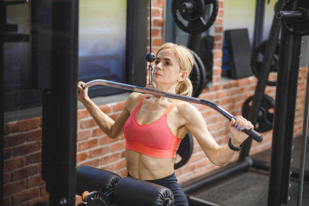 istock Woman working out in the gym on exercise machine, holding bar and pulling down 1450268035
