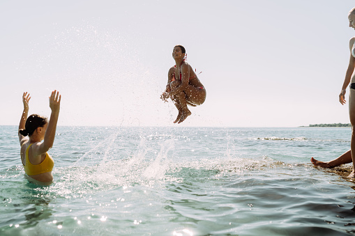 Photo of several friends jumping into the sea, having fun, and enjoying summer.