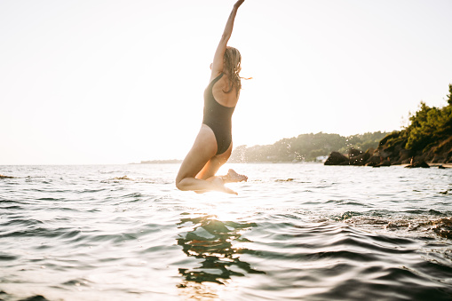 Photo of a young woman jumping into the ocean.