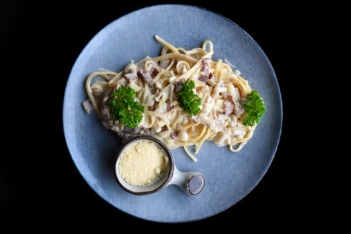 Pasta carbonara with bacon on blue plate isolated on black background top view