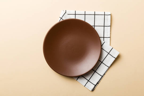 istock Top view on colored background empty round brown plate on tablecloth for food. Empty dish on napkin with space for your design 1450270403