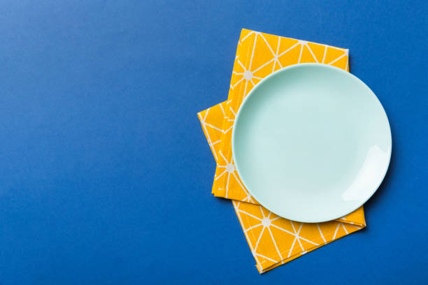 vista dall'alto su sfondo colorato piatto blu rotondo vuoto sulla tovaglia per il cibo. piatto vuoto sul tovagliolo con spazio per il tuo design - plate dinning table blue foto e immagini stock