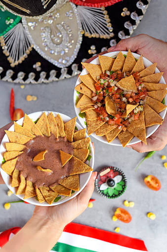 Hands holiding plates with Totopos tortilla with bean sauce and  pico de gallo