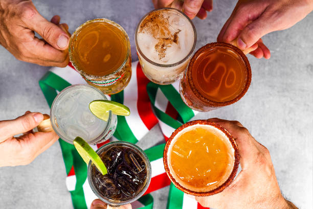 Hands holding mexican drinks making clink against mexican flag stock photo