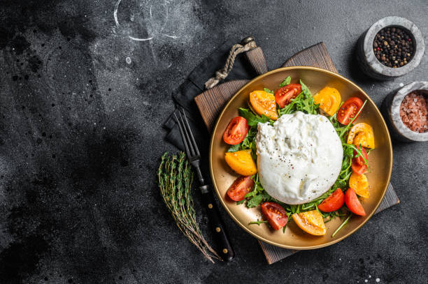 Burrata cheese with cherry tomatoes and fresh arugula in a plate. Black background. Top view. Copy space