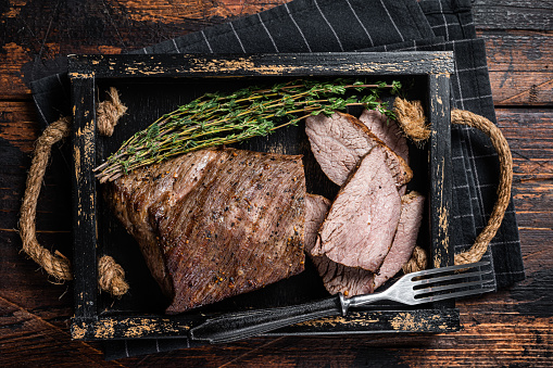 Grilled Tri Tip steak,  sirloin bottom beef in a tray with herbs. Wooden background. Top view.