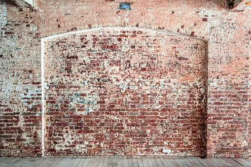 Weathered and distressed brick wall with arch feature in a warehouse with wooden floor