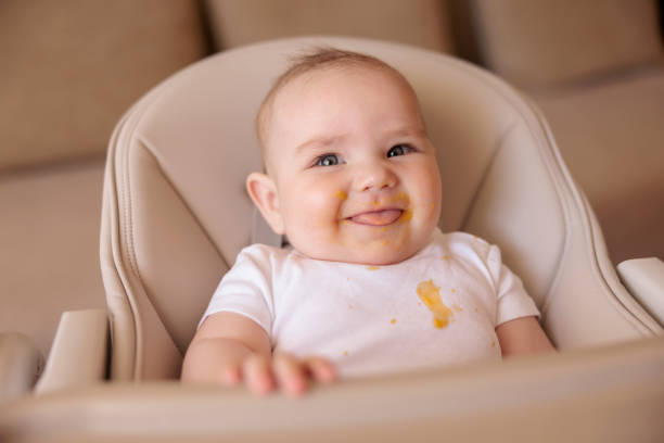 Cheerful baby boy playing in high chair after meal stock photo