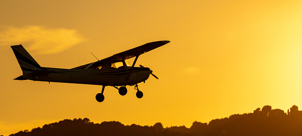 Silhouette of small propeller plane landing or taking off on the runway backlit under a yellow sun with the mountain below at sunset in Sabadell airport.