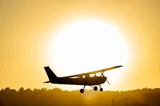 Silhouette of a small propeller plane landing or taking off on the runway backlit under a yellow sun at sunset at Sabadell airport.