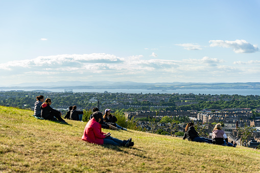 Edinburgh, Scotland, United kingdom - 06/19/2022: People stretched out on the grass of a mountain hill watching the views of the city of Edinburgh, UK.