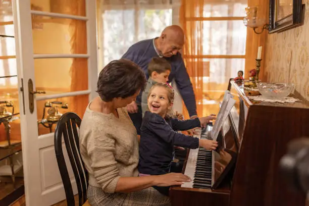 Mature woman playing a piano at home, with her is her family, niece, nephew and father.