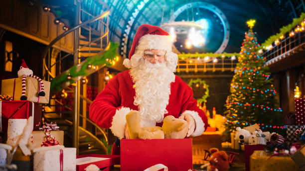 taller de santa claus en estudio: envolver y empacar regalos de navidad para todos los niños buenos que se entregarán en la víspera mágica de año nuevo. prepara el oso de peluche como regalo para un niño emocionado - workshop santa claus christmas north pole fotografías e imágenes de stock