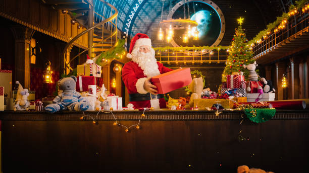 jolly santa claus en su taller de estudio: envolver y empacar regalos de navidad para todos los niños buenos que se entregarán en la víspera mágica de año nuevo. prepara los regalos estas vacaciones de invierno - workshop santa claus christmas north pole fotografías e imágenes de stock