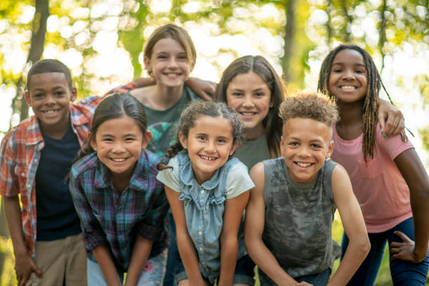 Children Outside A large group of school aged children huddle together outside for a portrait.  They are each dressed casually and are laughing and smiling as they enjoy each others company. 12 13 years stock pictures, royalty-free photos & images