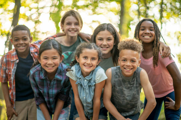 Children Outside A large group of school aged children huddle together outside for a portrait. They are each dressed casually and are laughing and smiling as they enjoy each others company. mixed racial group of friendly children laughing together stock pictures, royalty-free photos & images