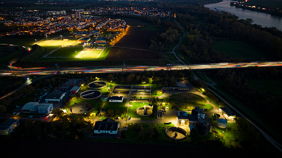 Illuminated sewage treatment plant and highway at dusk - aerial view, long exposure