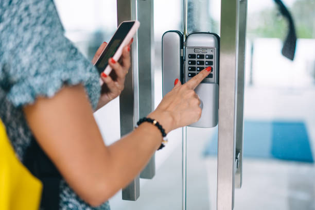 Cropped image of female holding mobile phone using modern app for getting security code for entering smart home, woman pressing secret number on button of keypad control near door for disarming imagen recortada de una mujer sosteniendo un teléfono móvil usando una aplicación moderna para obtener un código de seguridad para ingresar a una casa inteligente, una mujer presionando el número secreto en el botón del control del teclado cerca de l