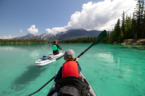 A Mother and son are paddleboarding on Edith Lake  in Jasper National Park, Alberta. The turquoise colored lake is very calm. Its is a beautiful sunny summer day in the Canadian Rockies.