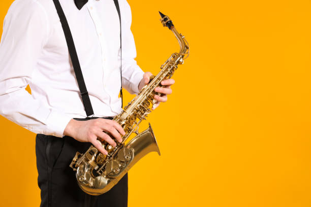 istock Man in elegant outfit with saxophone on yellow background, closeup. Space for text 1450326682
