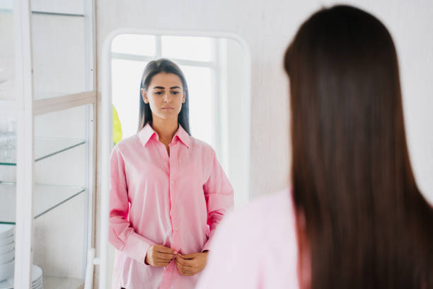 Sad brunette fit young woman in pink oversize shirt stands in front of mirror feels loneliness. Frustrated hispanic girl in troubles standing on kitchen. Diet and health care. Dietetics. Fasting Sad brunette fit young woman in pink oversize shirt stands in front of mirror feels loneliness. Frustrated hispanic girl in troubles standing on kitchen. Diet and health care. Dietetics. Fasting low self esteem stock pictures, royalty-free photos & images