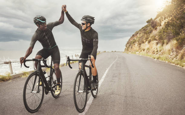 fahrrad, freunde und männer high five auf der straße haben spaß beim radfahren im freien. erfolg, vielfalt und teamwork von männlichen radfahrern auf fahrrädern auf der straße, bewegung oder workout-training auf asphalt. - bicycle racer stock-fotos und bilder