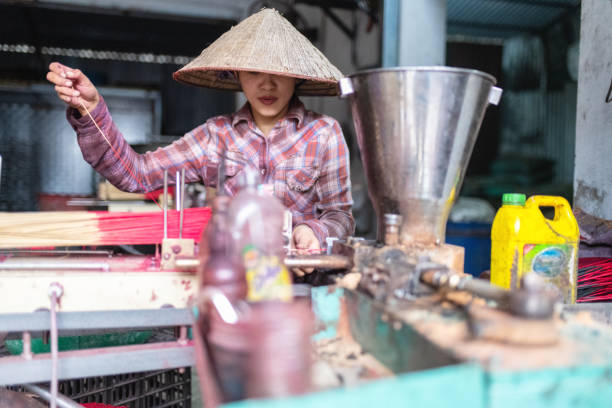 front view on vietnamese woman sitting at work bench producing red incense sticks at work bench