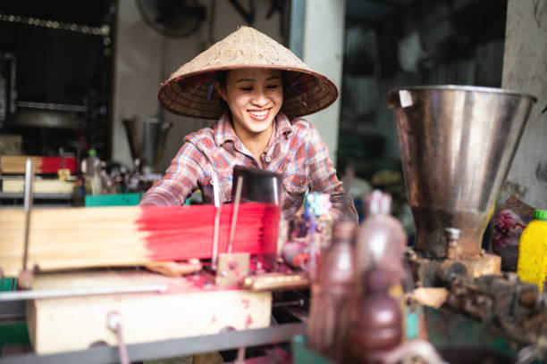 smiling vietnamese woman sitting behind workbench with tools for manufacturing incense sticks
