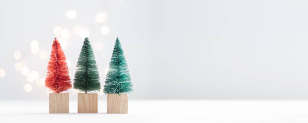 istock Cute Christmas miniature fir trees on a white table with bokeh lights 1450331127