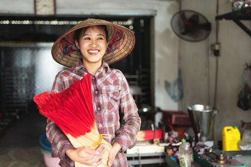 portrait of smiling vietnamese woman holding bundle of red incense sticks in her hands