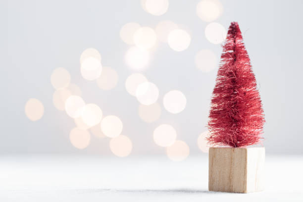 istock Cute Christmas miniature fir tree on a white table with bokeh lights 1450331392