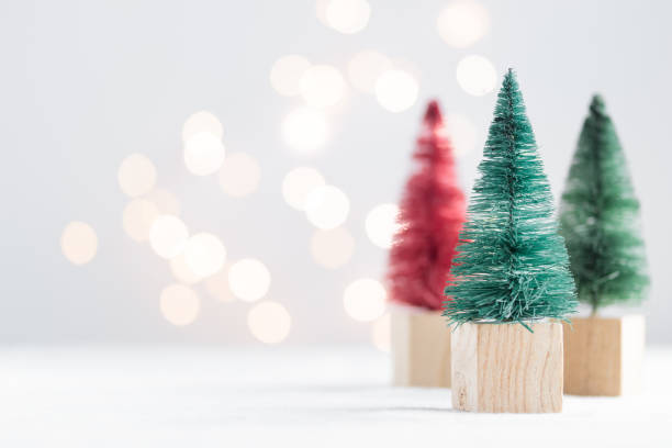 istock Cute Christmas miniature fir trees on a white table with bokeh lights 1450331408