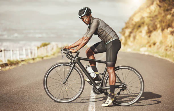 radfahren, energie und fahrrad radfahrer auf einer straße entlang eines berges, kraft, fokus und denkweise in südafrika. sport-, fitness- und marathontraining mit schwarzem mann, der mit dem fahrrad entlang der aussicht auf die stadt fährt - endurance sport stock-fotos und bilder