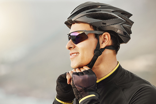 Fitness, sports and cyclist checking his helmet before cycling, training, workout and cardio ride in nature. Health, biking and athletic man getting ready for cycle, happy, smile and relaxed training