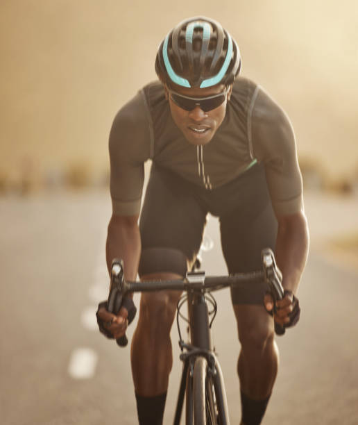 Fitness, sports and cycling man workout in a road at sunset, health, wellness and morning cardio exercise. Energy, speed and focus power by athletic black man cycling on bicycle for marathon training fitness, deportes y ciclismo hombre ejercicio en una carretera al atardecer, salud, bienestar y ejercicio cardiovascular matutino. energía, velocidad y poder de concentración por un hombre negro atlético que anda en bicicleta para el entrenamiento de ma