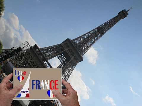 Hands holding a Love Paris France postcard in front of the Eiffel Tower