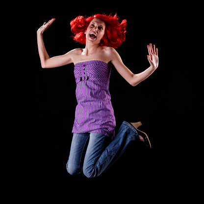 Jumping cute redhaired young woman mid-air on black background.