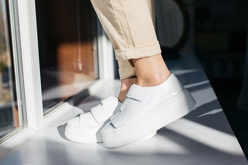 A pair of stylish sneakers. The girl is wearing a pair of white leather sneakers. Indoor photo. Close-up.