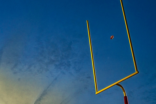 Making a field goal or extra point through the goal post during an American football game at night as the sun sets.