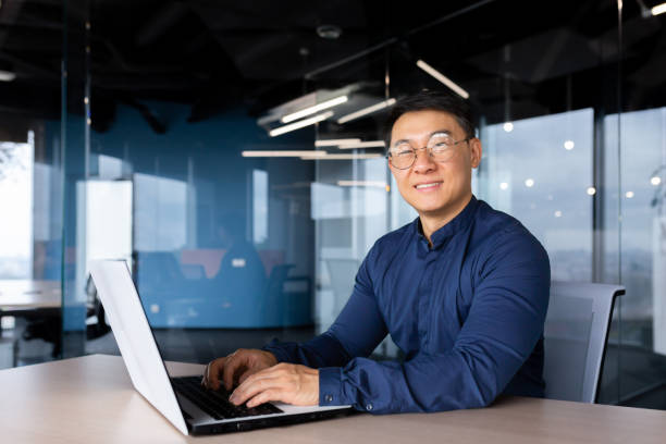 istock Successful asian businessman smiling and looking at camera, programmer porter inside office using laptop writing code for software security 1450340131