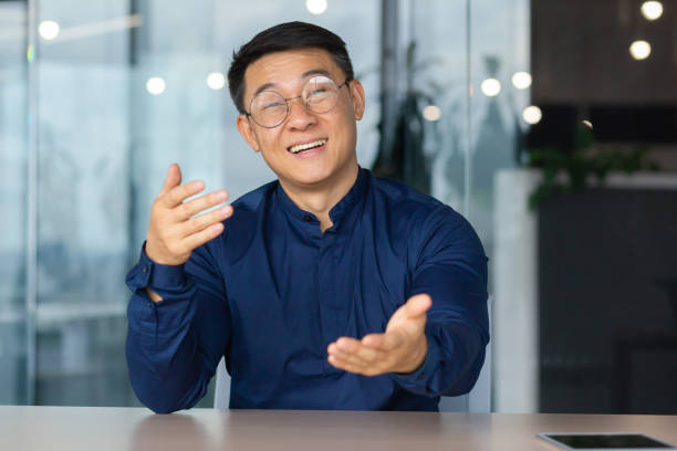 istock Video call online meeting asian businessman looking web camera and having fun talking and gesturing, man working inside office sharing plans with partners and colleagues, boss in shirt and glasses 1450340334