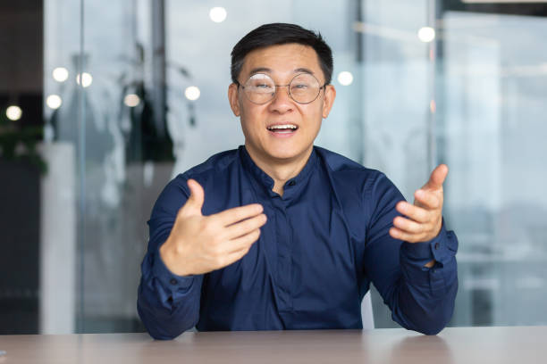 istock Video call online meeting asian businessman looking web camera and having fun talking and gesturing, man working inside office sharing plans with partners and colleagues, boss in shirt and glasses 1450340367
