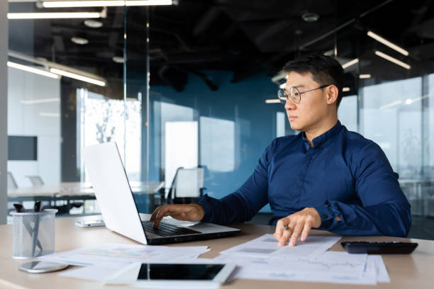Mature Asian businessman works with documents and calculates bills uses calculator, auditor checks contracts and financial papers serious and focused Mature Asian businessman works with documents and calculates bills uses calculator, auditor checks contracts and financial papers serious and focused. taiwan people stock pictures, royalty-free photos & images