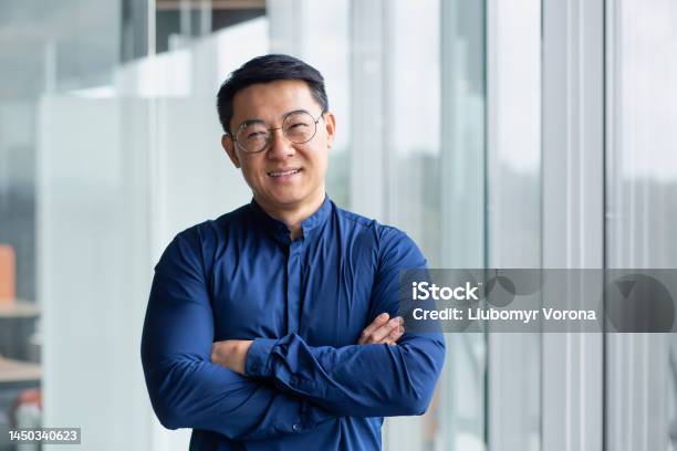 Portrait Of Successful Mature Boss Senior Businessman In Glasses Asian Looking At Camera And Smiling Man With Crossed Arms Working Inside Modern Office Building Stock Photo - Download Image Now